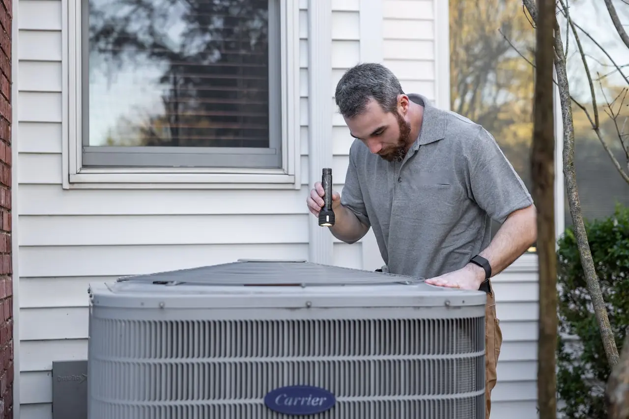Climate Heroes HVAC technician in a polo shirt inspecting a residential air conditioning unit outside an Alpharetta home